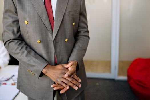 A businessman in a suit clasping hands indoors, professional and confident.