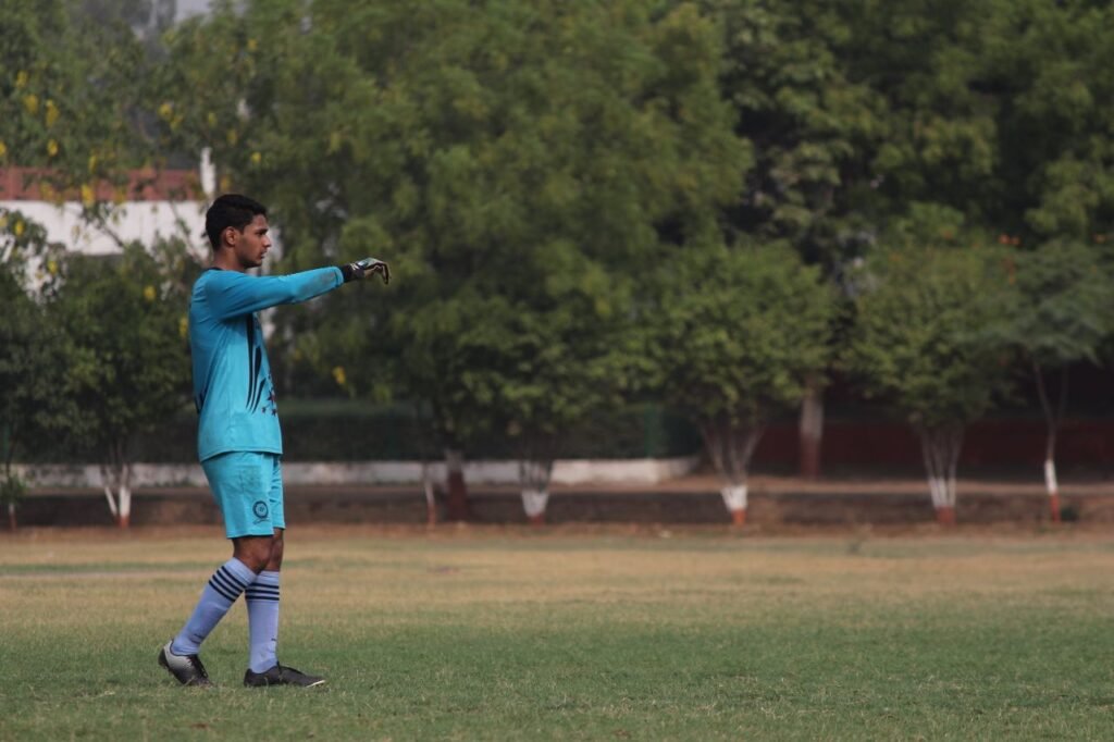 Teen soccer player in goalie uniform on a lush outdoor field.