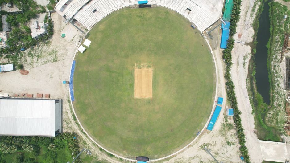 Top-down view of a cricket stadium in Dhaka, showcasing the pitch and surrounding areas.