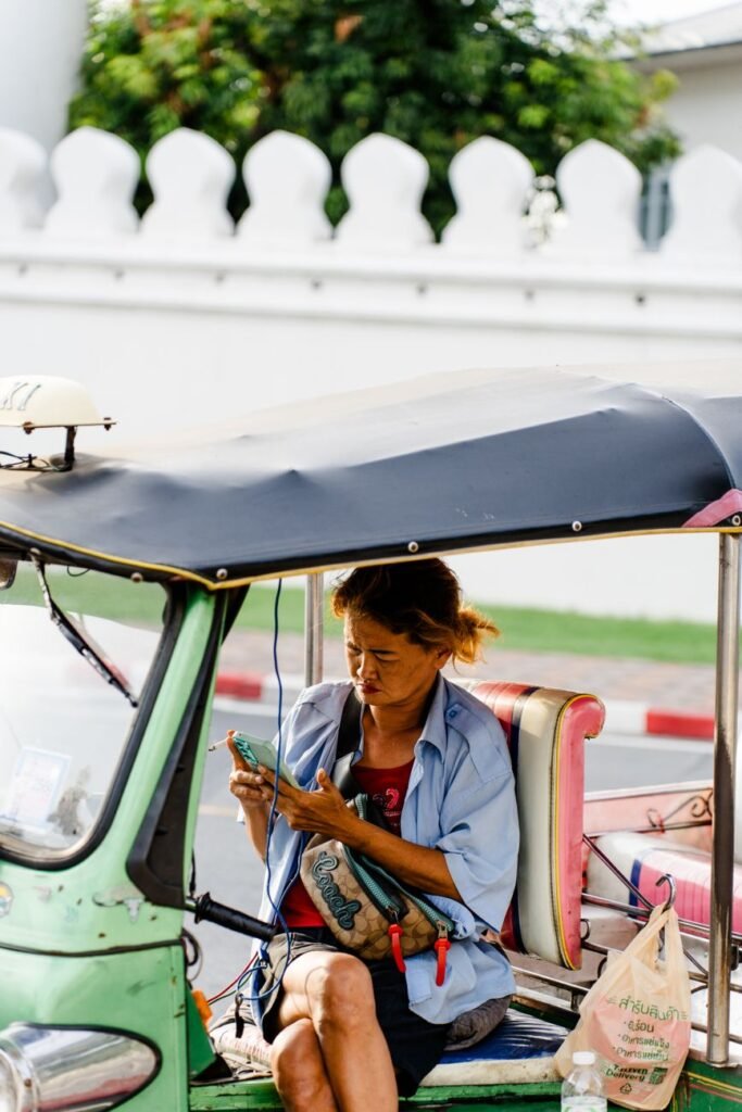Woman sitting in a tuk tuk using a smartphone on a sunny day. Urban transport setting.