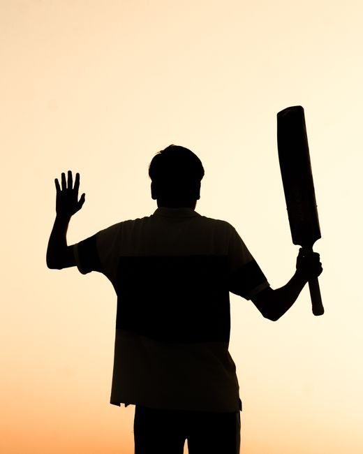 Silhouette of a person holding a cricket bat against a warm sunset sky in India.
