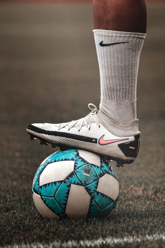 A person in sportswear balancing a blue soccer ball on grassy field.