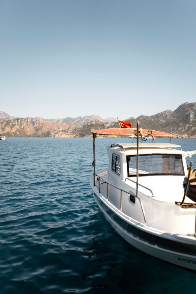 White fishing boat on calm Mediterranean sea with mountains under clear blue sky.