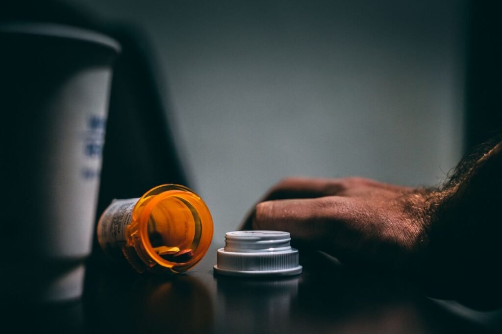 Moodily lit scene of an open prescription bottle and hand on a table, depicting healthcare themes.