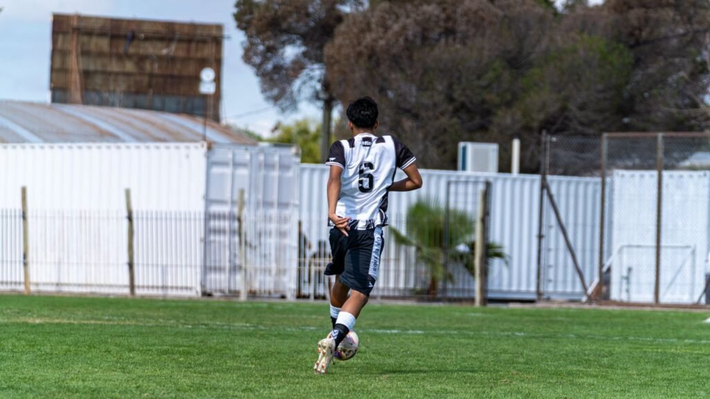 A teenage soccer player wearing number six dribbles the ball outdoors in a park.