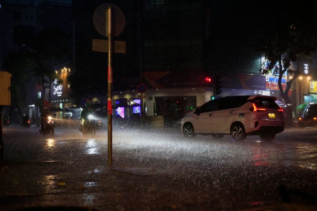 Nighttime rain pours down on a busy street in Ho Chi Minh City, Vietnam, capturing urban life.