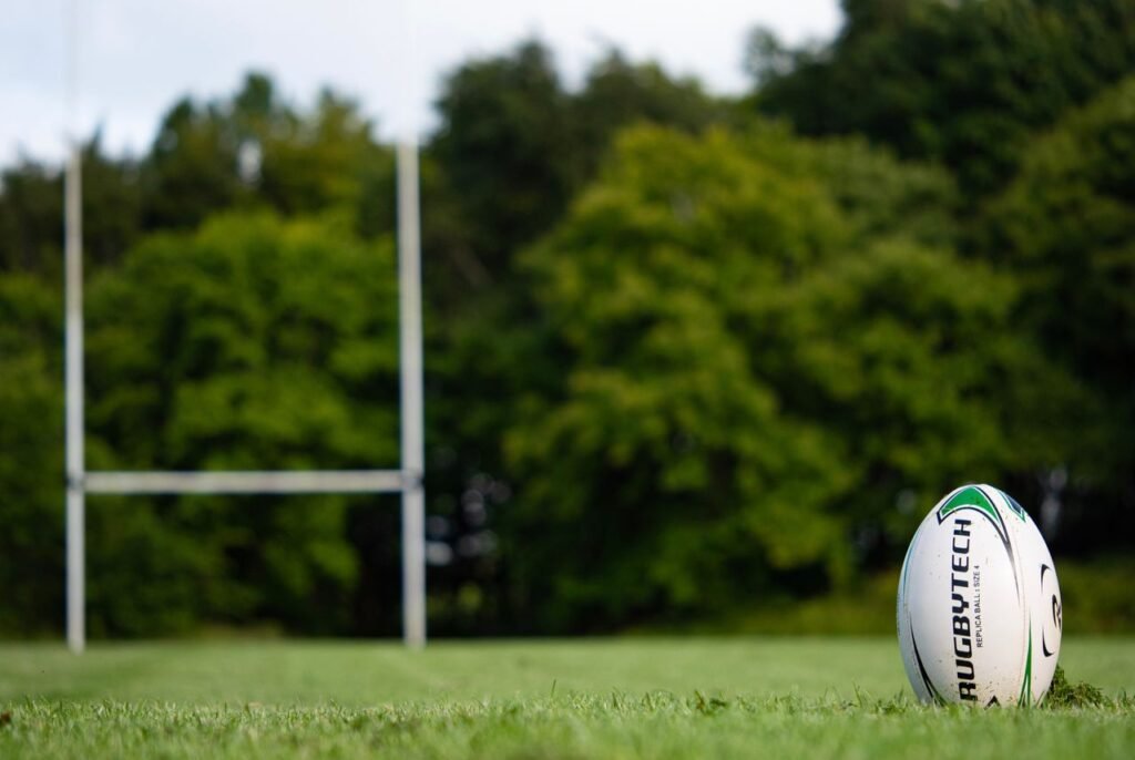 Rugby ball resting on a field in Galway, Ireland with goalposts in the background.